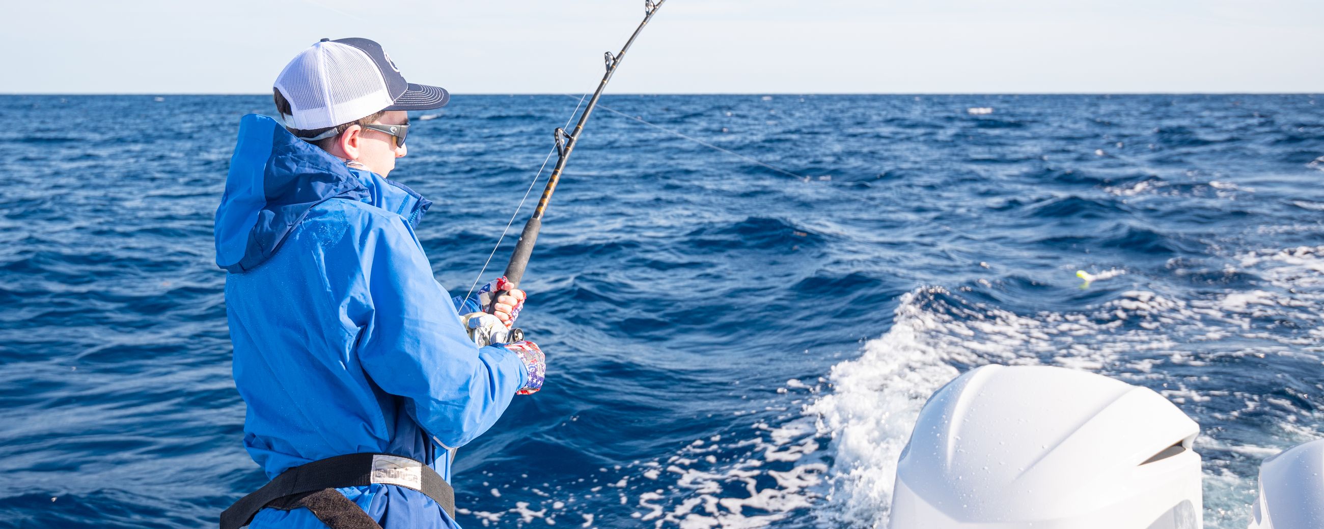 Young boy reeling in a fish offshore wearing a blue jacket